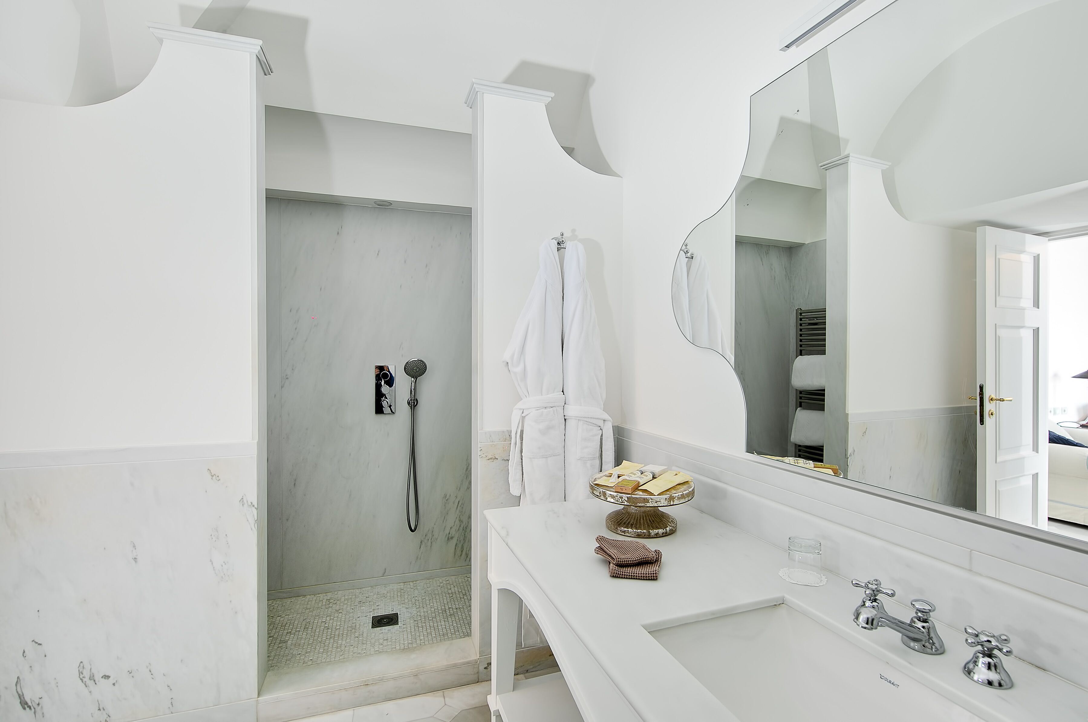Un bagno moderno con cabina doccia, un ampio specchio e un piano di lavoro in marmo.