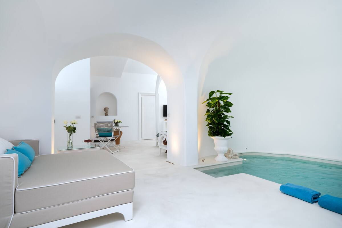 A modern, minimalist hotel room with a large window, a cozy seating area, and a small pool.