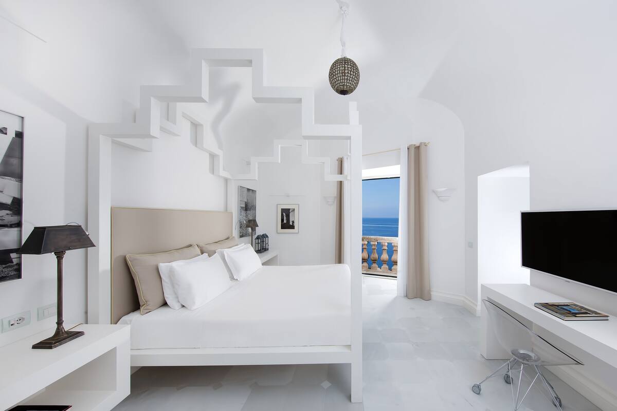 A modern bedroom with a bed, bedside table, lamp, and a TV.