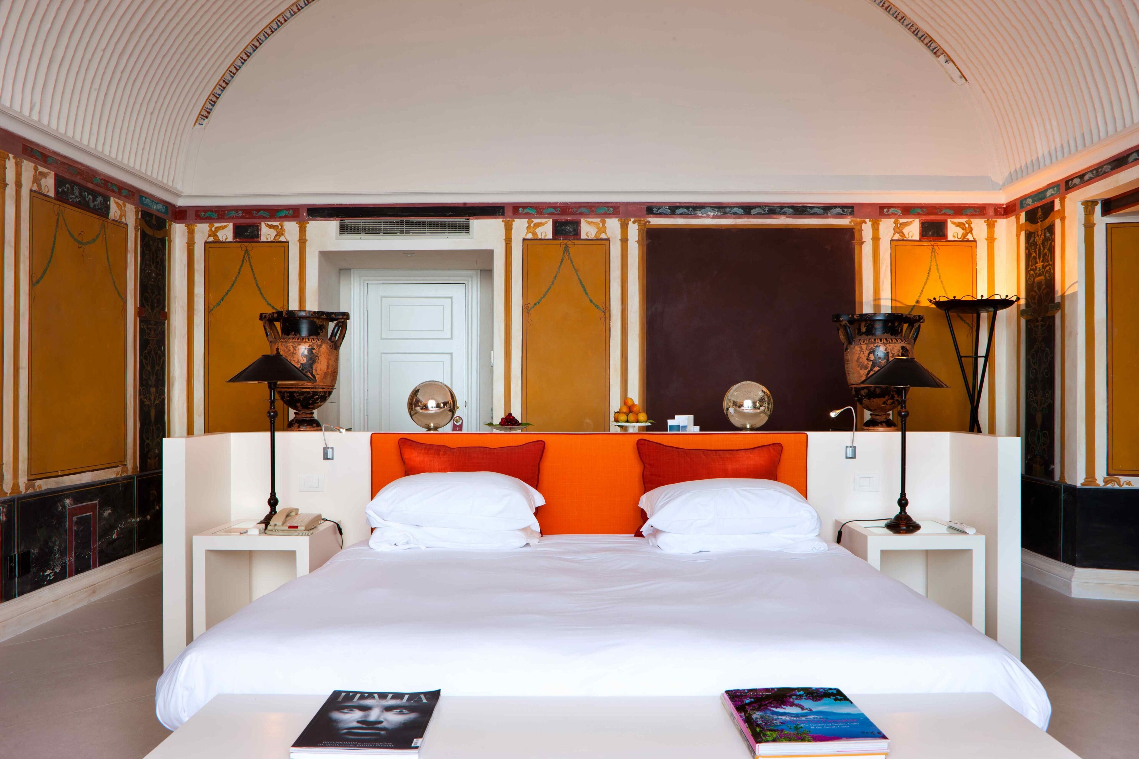 A hotel room with a large bed, two nightstands, a white door, and decorative wall sconces.