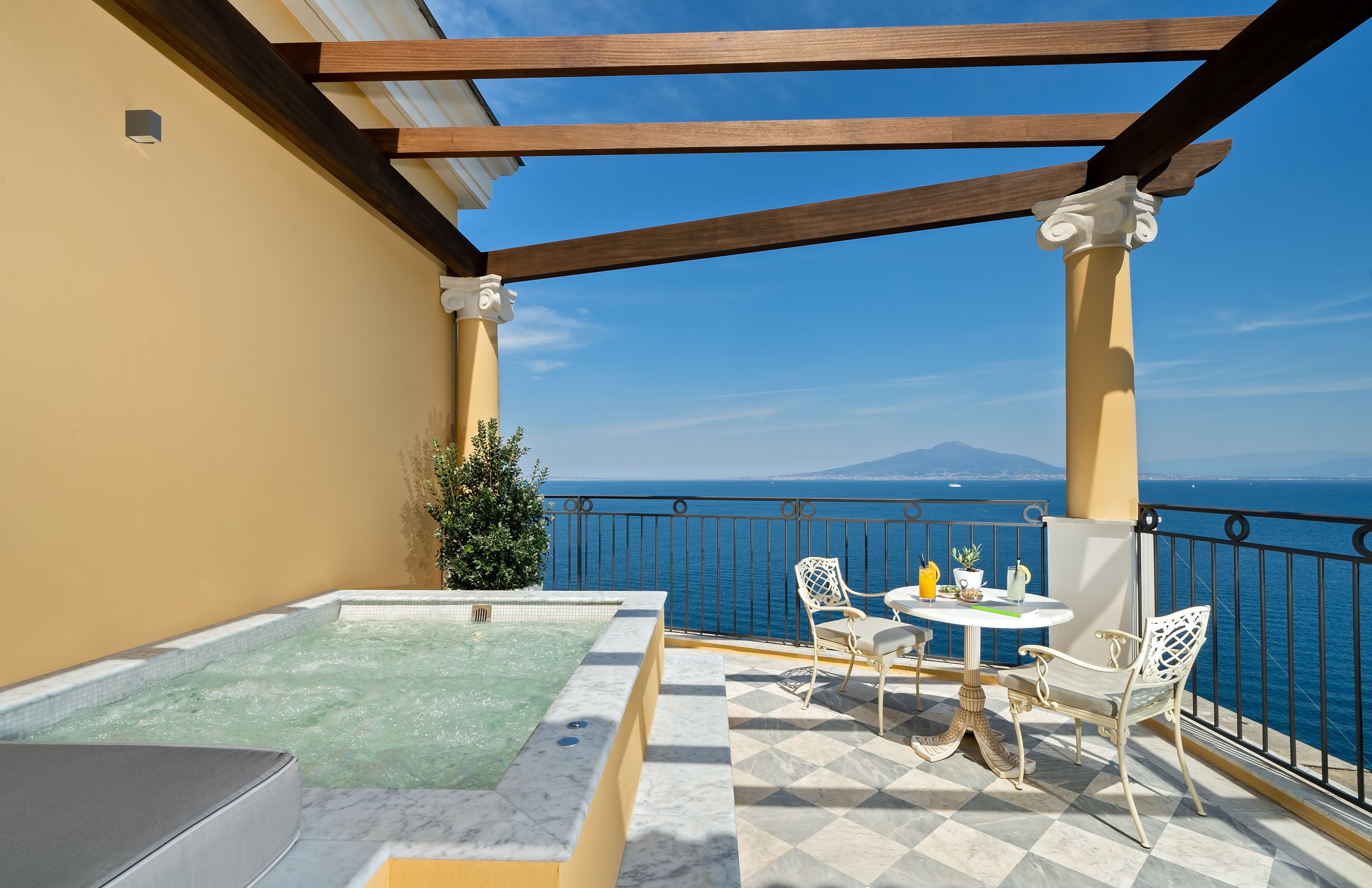 A balcony with a hot tub, seating, and a view of the sea.