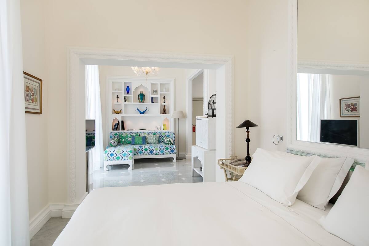 A bedroom with a large bed, a white wardrobe, a colorful sofa, and a mirror.