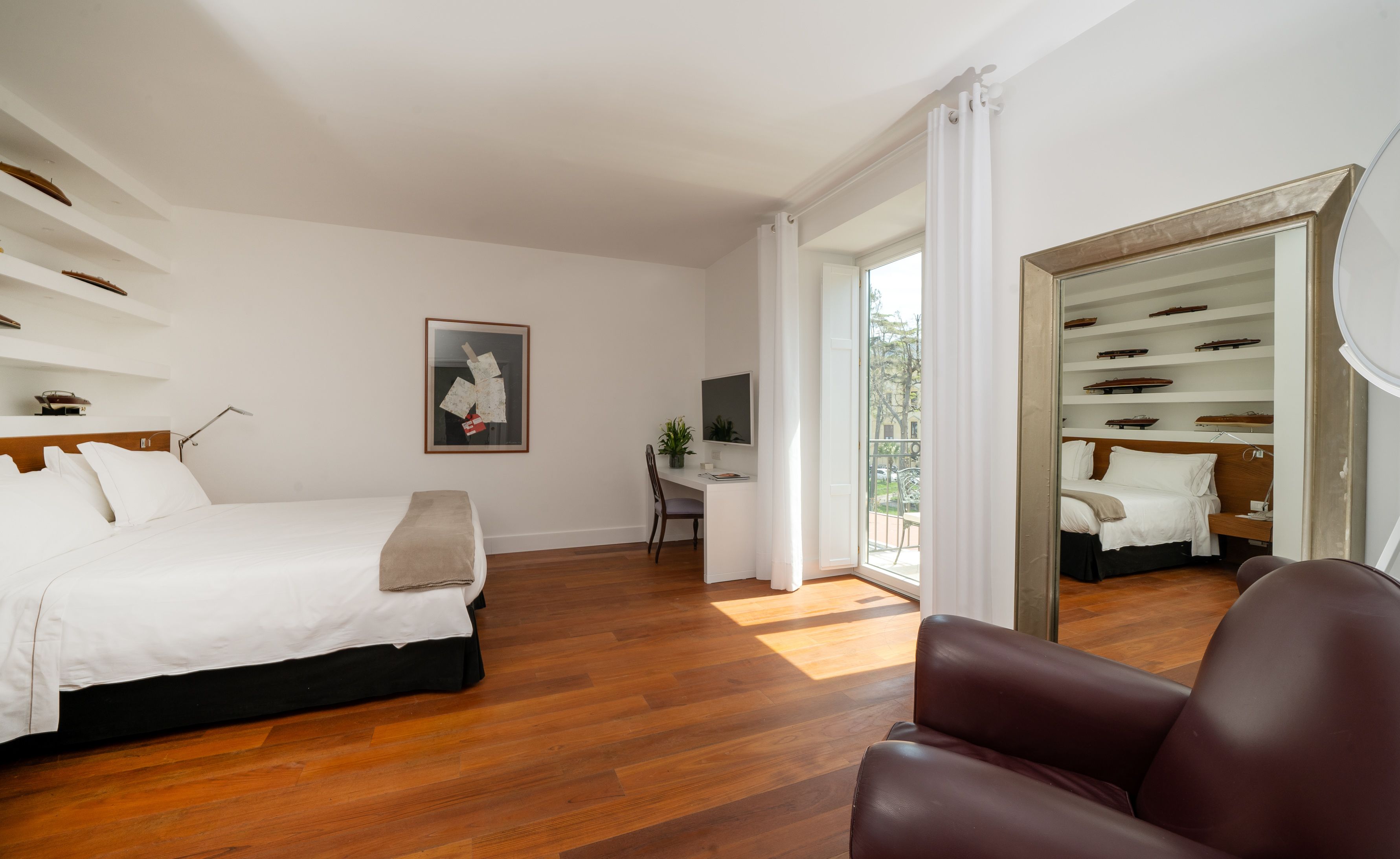 Une chambre d’hôtel moderne avec un grand lit, un bureau et une chaise. Une grande fenêtre offre une vue sur l’extérieur.