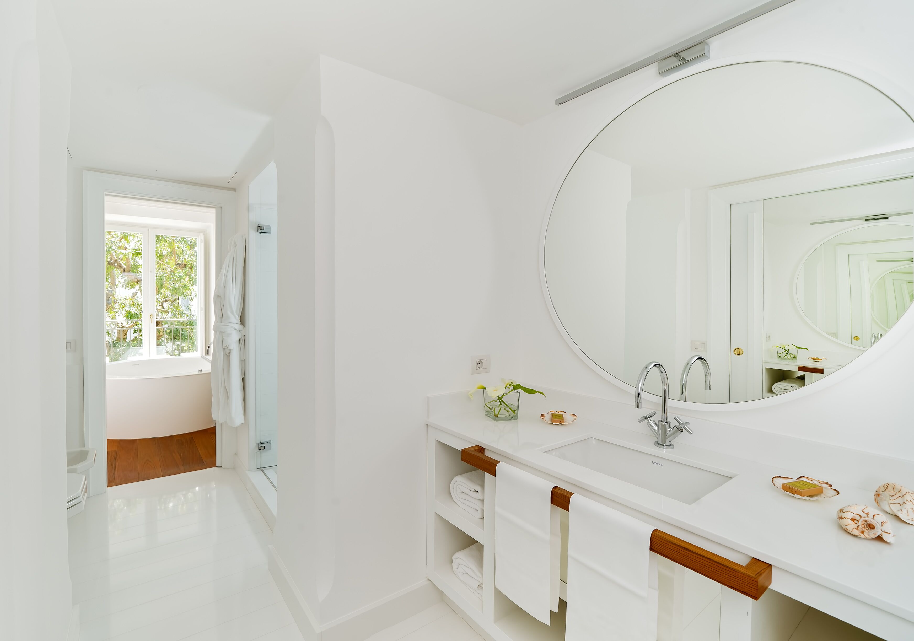 A modern bathroom with a large mirror, white fixtures, and a view to a wooden floor.