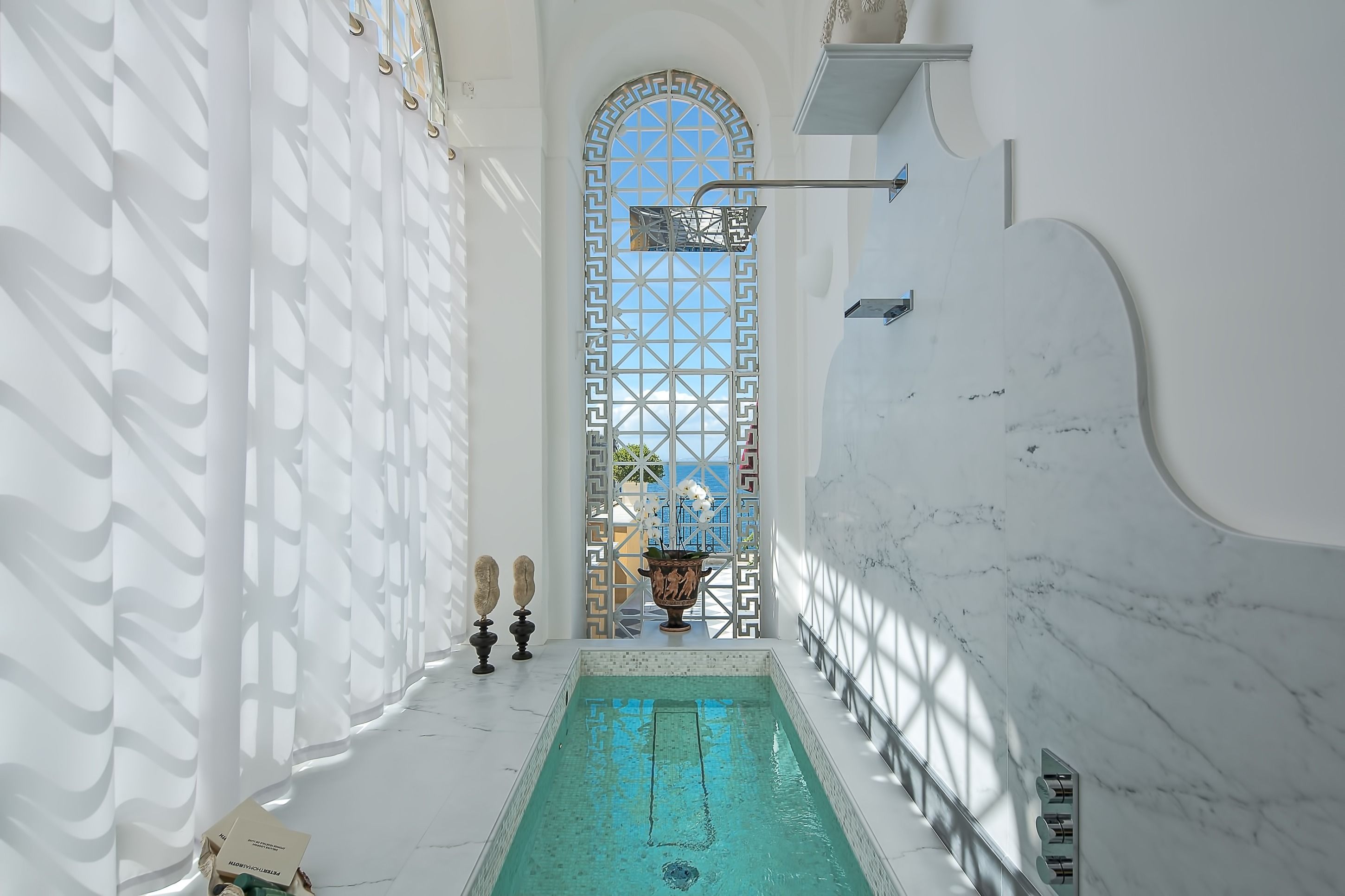 Un espace piscine offrant une vue dégagée sur le ciel grâce à une fenêtre décorative, le tout entouré de murs blancs et d’un sol en marbre.