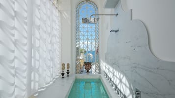 Un espace piscine offrant une vue dégagée sur le ciel grâce à une fenêtre décorative, le tout entouré de murs blancs et d’un sol en marbre.