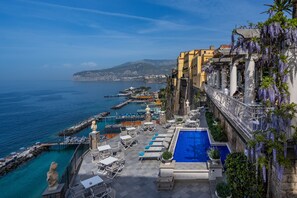 Un área de piscina en la azotea con vista al mar, mobiliario exterior y una estatua.