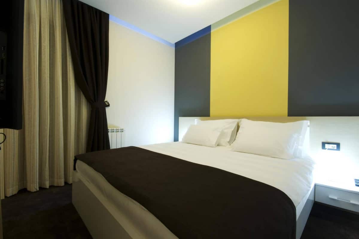 A hotel room with a bed, curtains, a bedside table, and a wall with a geometric design.