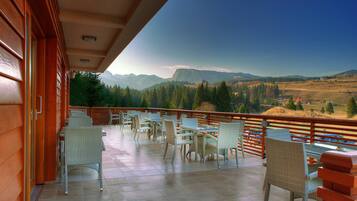 A balcony with wicker chairs and tables, overlooking a mountainous landscape.