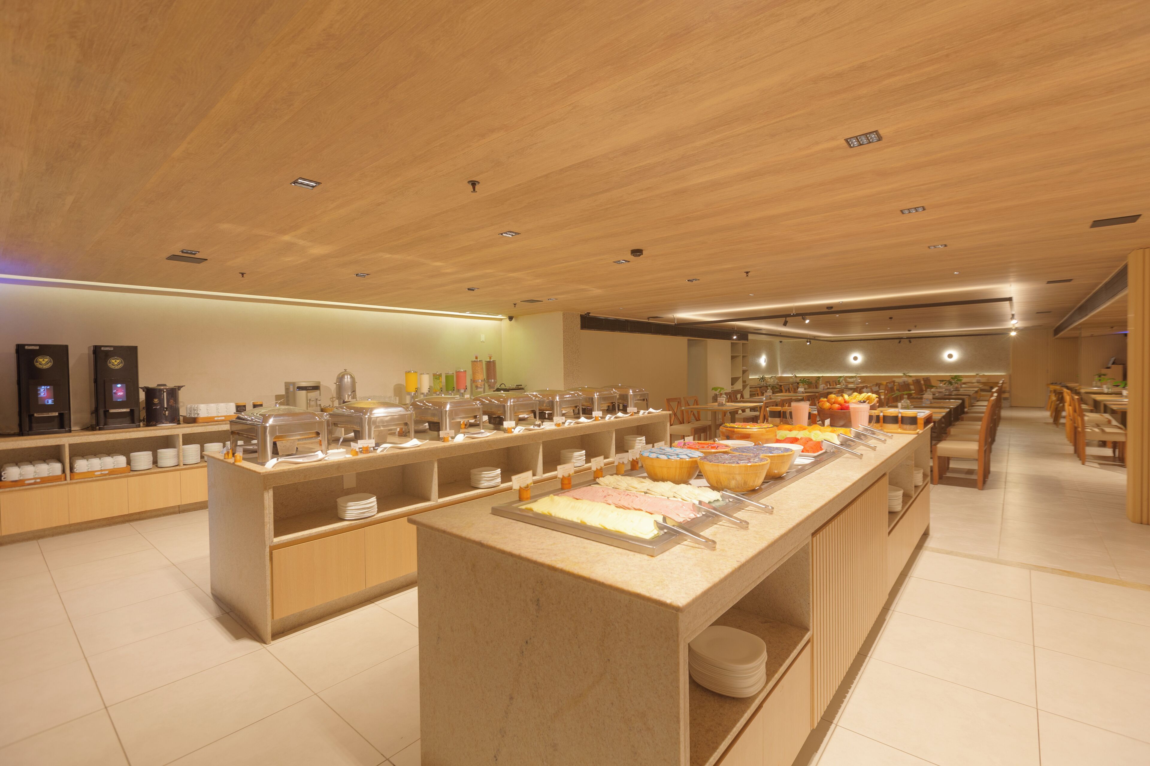 Zona de bufé con varias estaciones de comida, incluyendo una isla central con una variedad de platos y una barra larga con opciones adicionales.