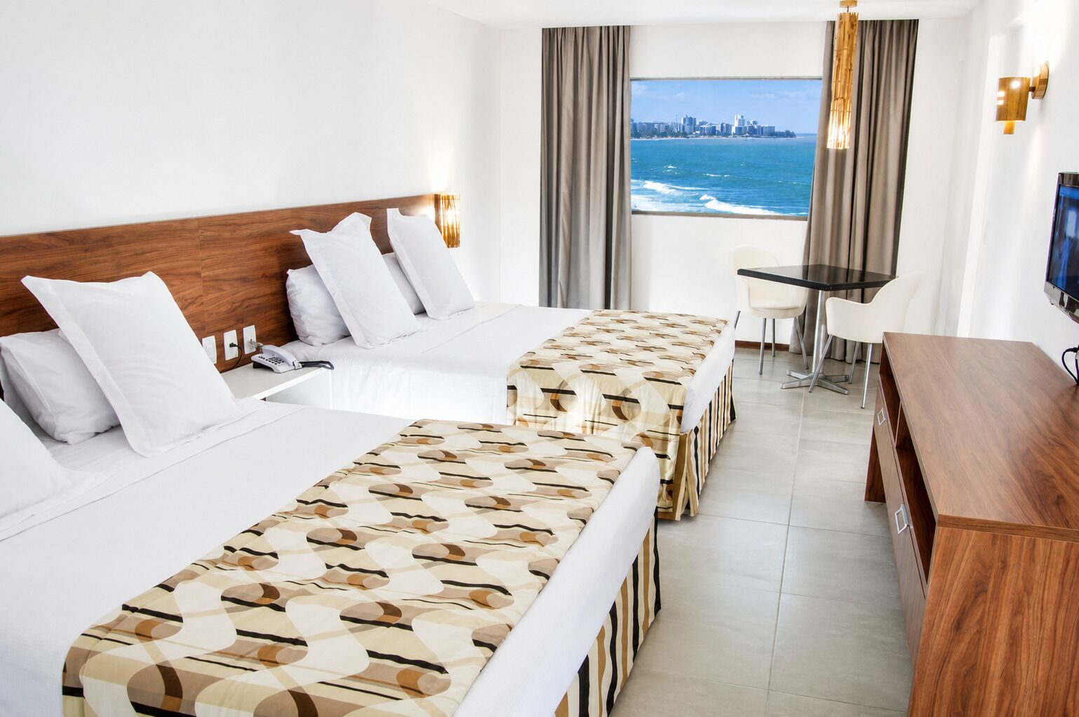 Habitación de hotel con dos camas, un escritorio, una silla y vista al océano.