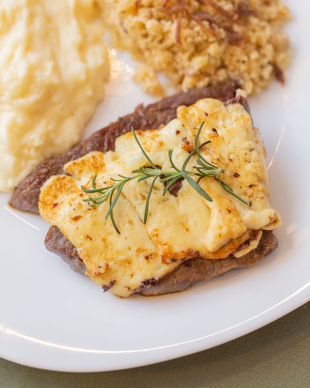 Ein Teller mit einem Steak, überzogen mit Käse, dazu Kartoffelpüree.