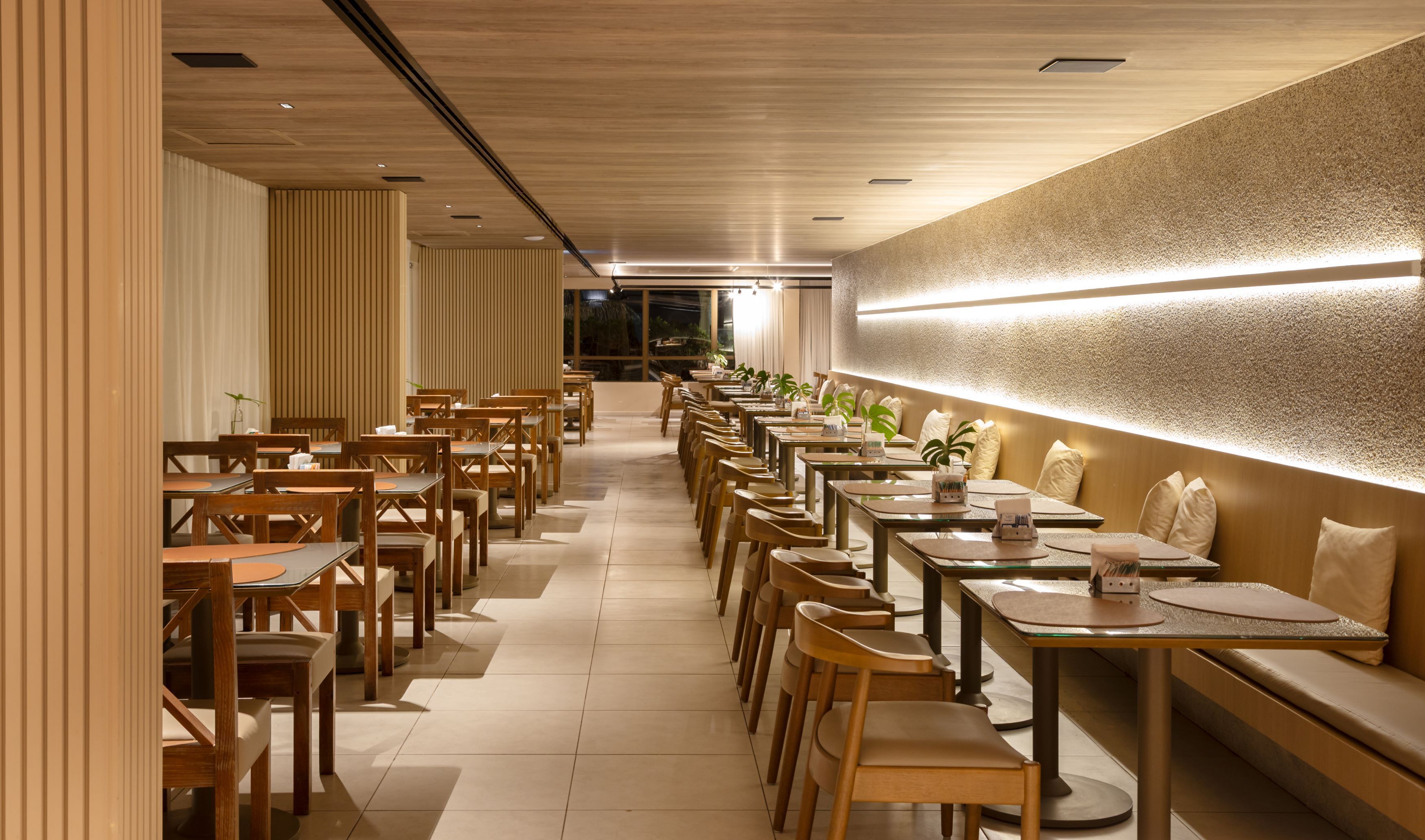 Um restaurante moderno com mesas e cadeiras de madeira, um balcão comprido e uma parede com textura.