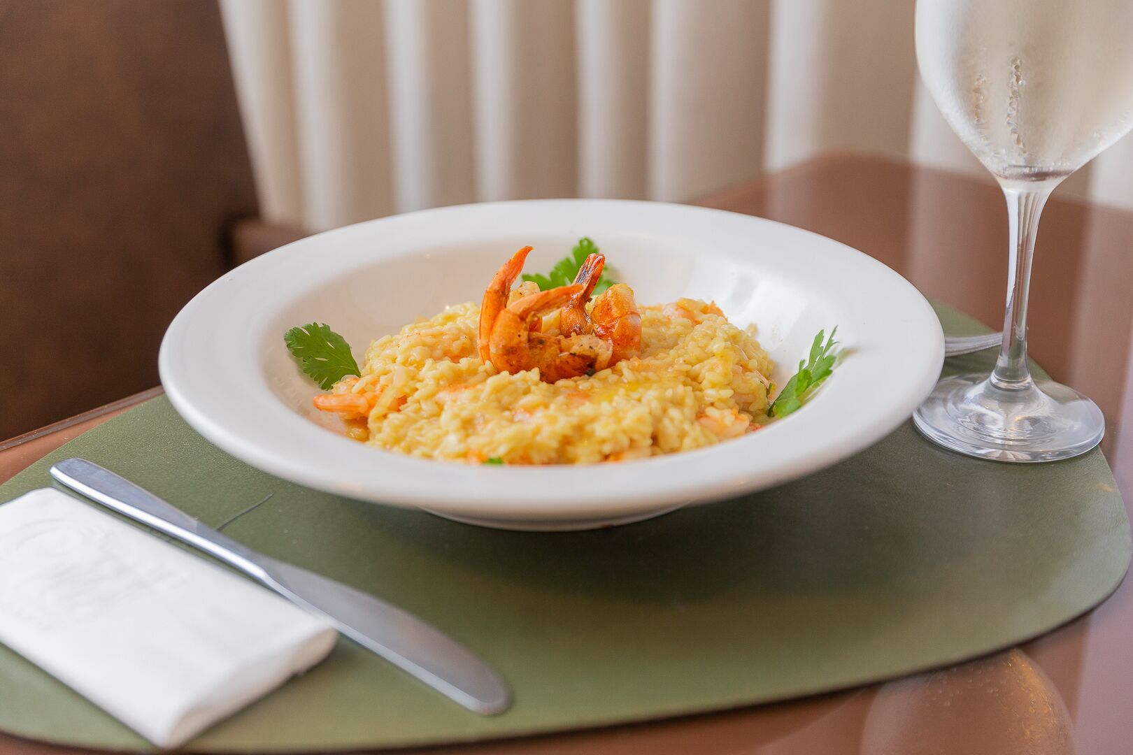 Um prato de risoto com camarões e decoração, um copo de água e um guardanapo sobre a mesa.