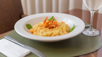 Um prato de risoto com camarões e decoração, um copo de água e um guardanapo sobre a mesa.