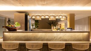 Un espace bar moderne doté d’un comptoir en marbre, de chaises en osier et de luminaires suspendus.