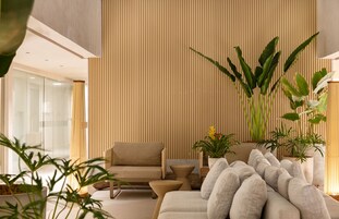 A modern living room with a sofa, armchairs, and a coffee table, featuring vertical wooden paneling and potted plants.