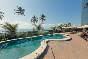 A pool area with a curved design, palm trees, and a view of the ocean.