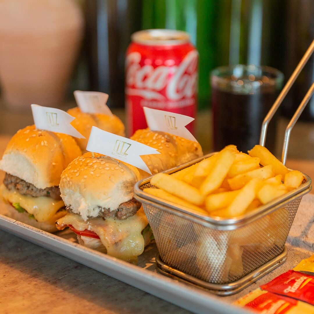 A tray with two burgers and a basket of fries, with a can of Coca-Cola in the background.