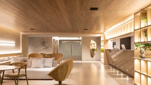 Un intérieur moderne avec un plafond en bois, un coin salon avec des fauteuils en osier, un canapé blanc et un comptoir d’accueil doté d’étagères.