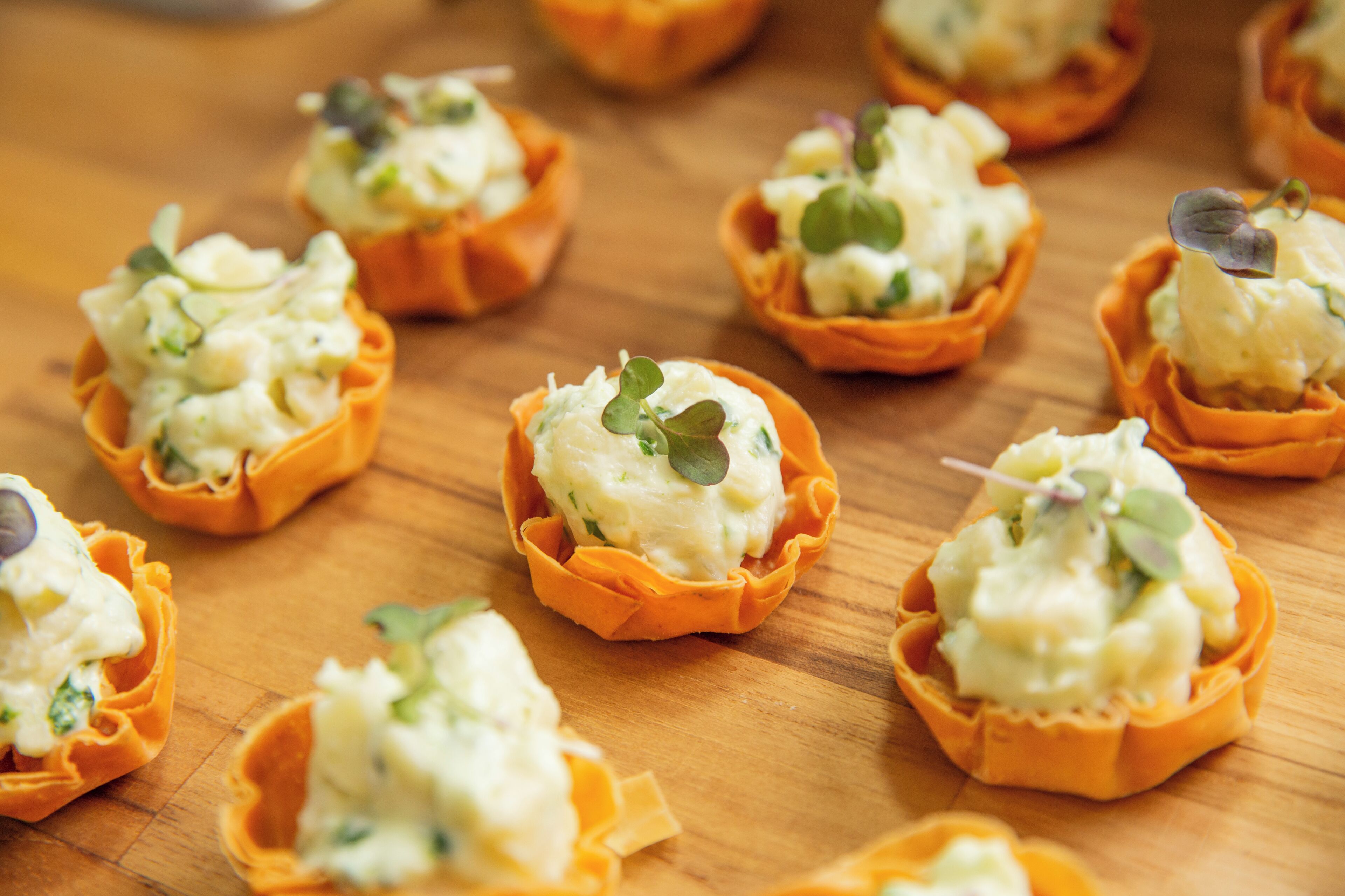 A wooden table with multiple orange tart shells filled with a creamy substance and garnished with green leaves.