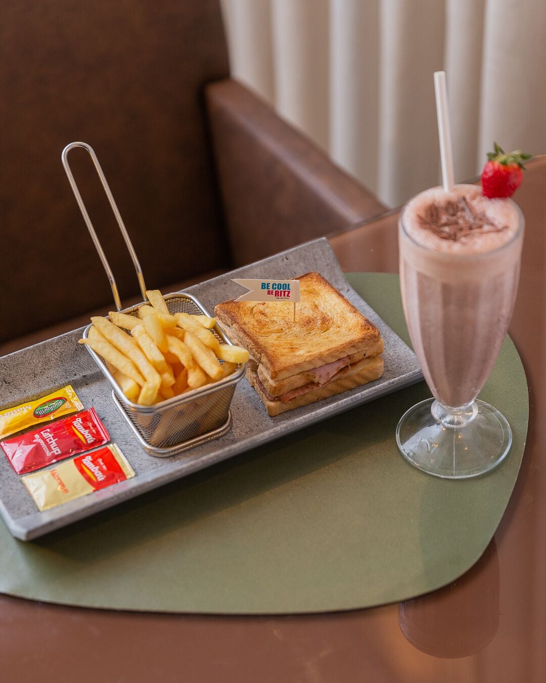 Una bandeja con un sándwich, papas fritas y una bebida sobre una mesa.