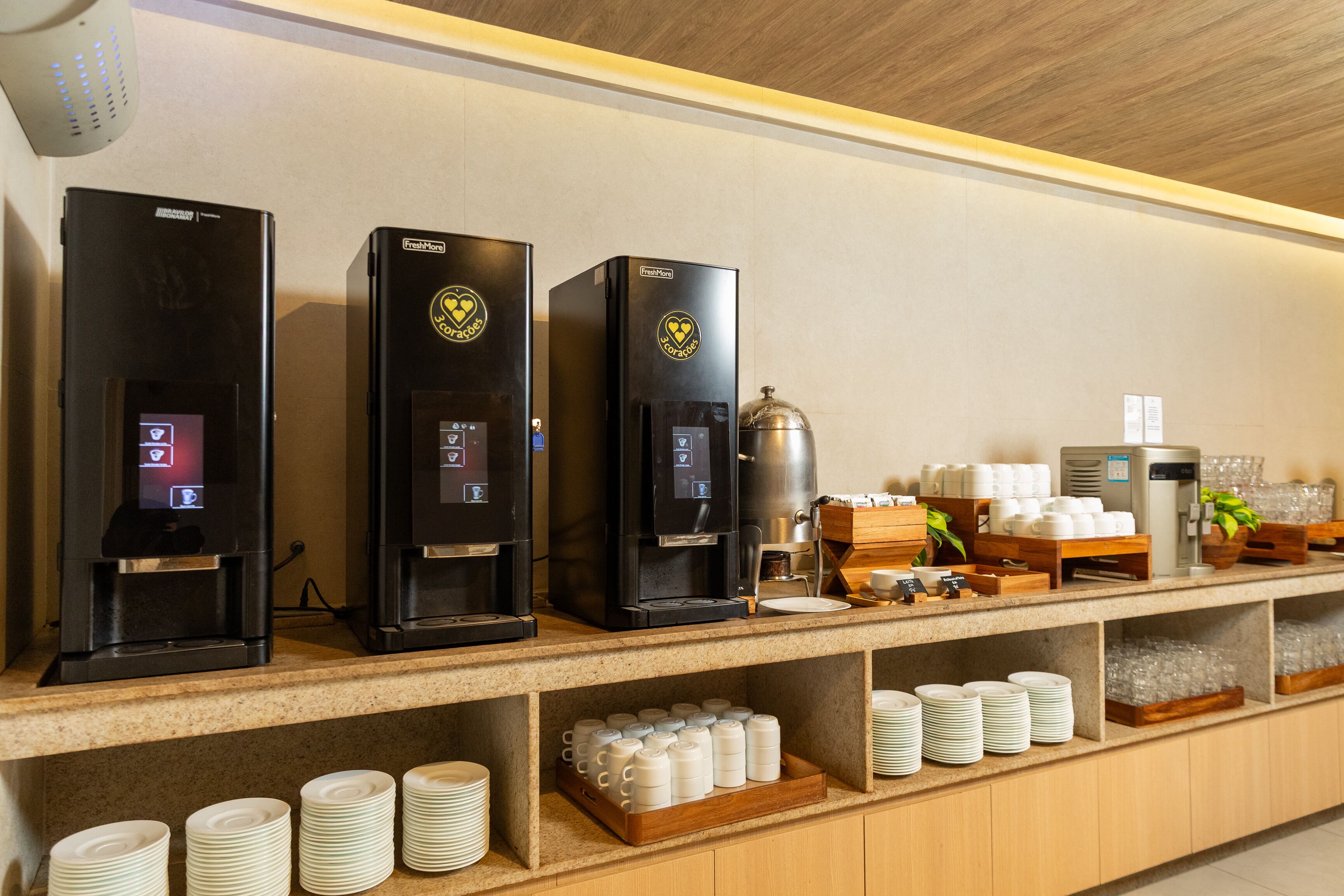 A coffee station with three espresso machines, a coffee pot, and a variety of coffee cups and saucers.
