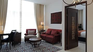 Habitación de hotel con sofá rojo, alfombra estampada, escritorio con silla y cama con cabecero decorado.