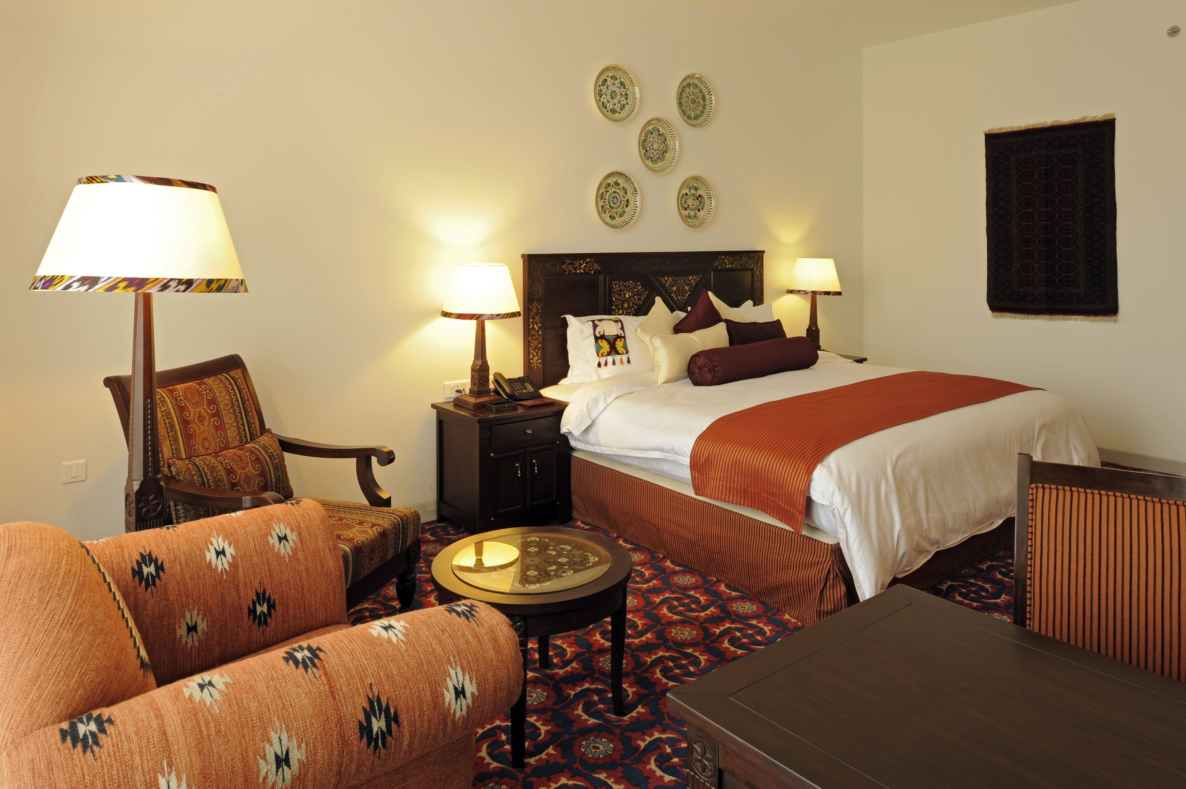 A hotel room with a bed, two bedside tables with lamps, a sofa, a small round table, and a patterned carpet.