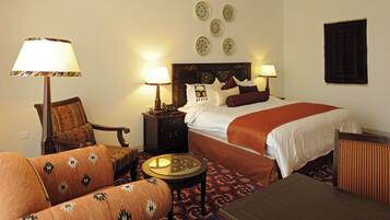 A hotel room with a bed, two bedside tables with lamps, a sofa, a small round table, and a patterned carpet.