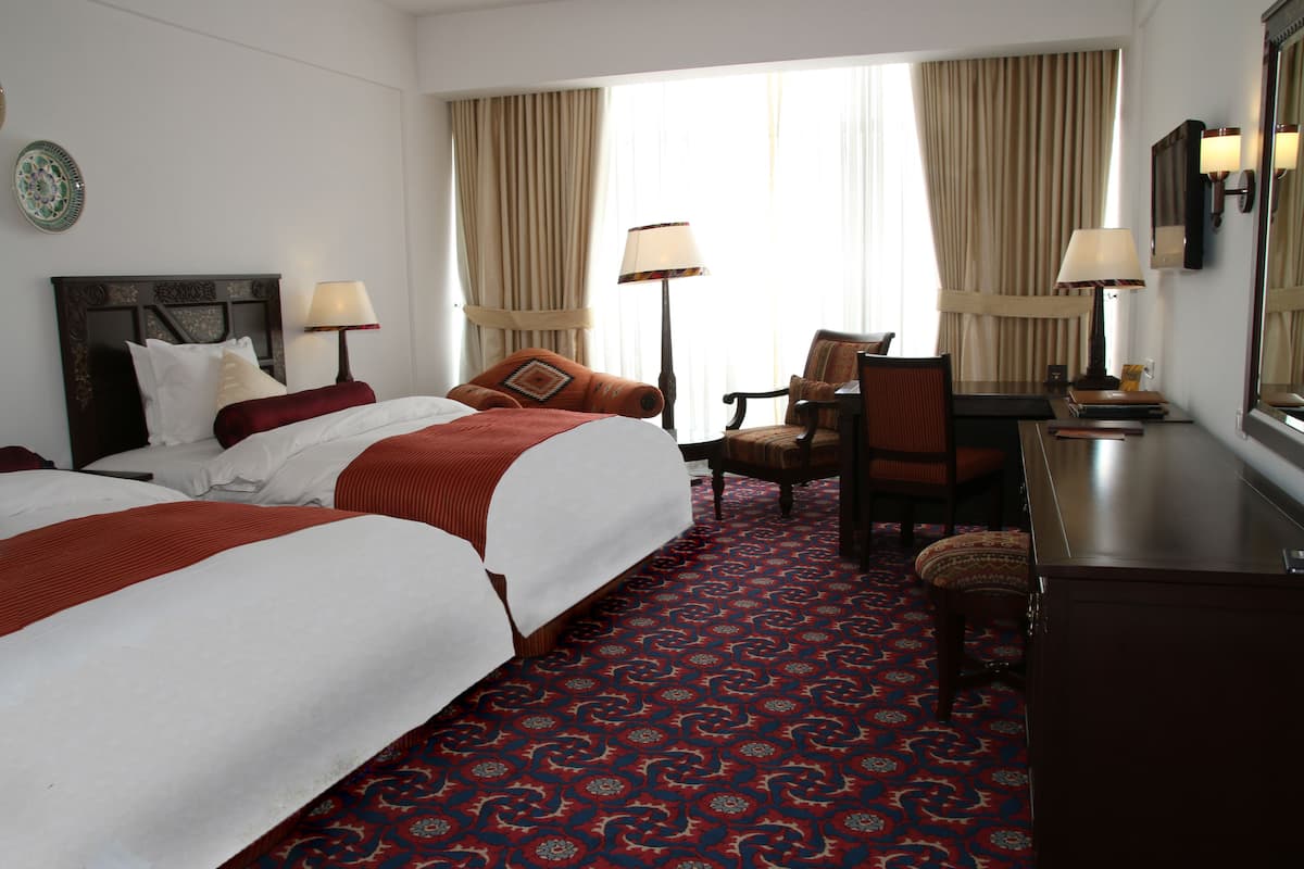 A hotel room with two beds, a desk, a chair, and a large window with curtains.