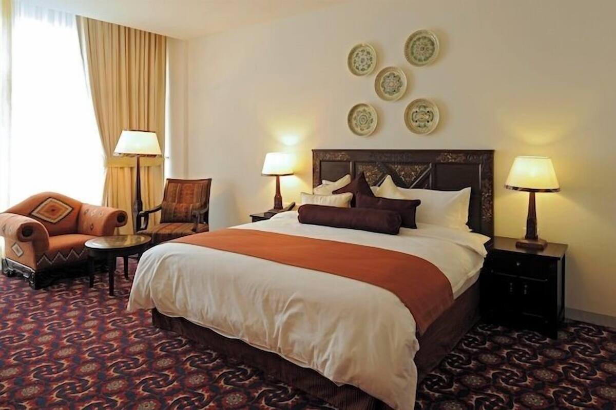 A hotel room with a large bed, two side tables with lamps, a sofa, and a patterned carpet.