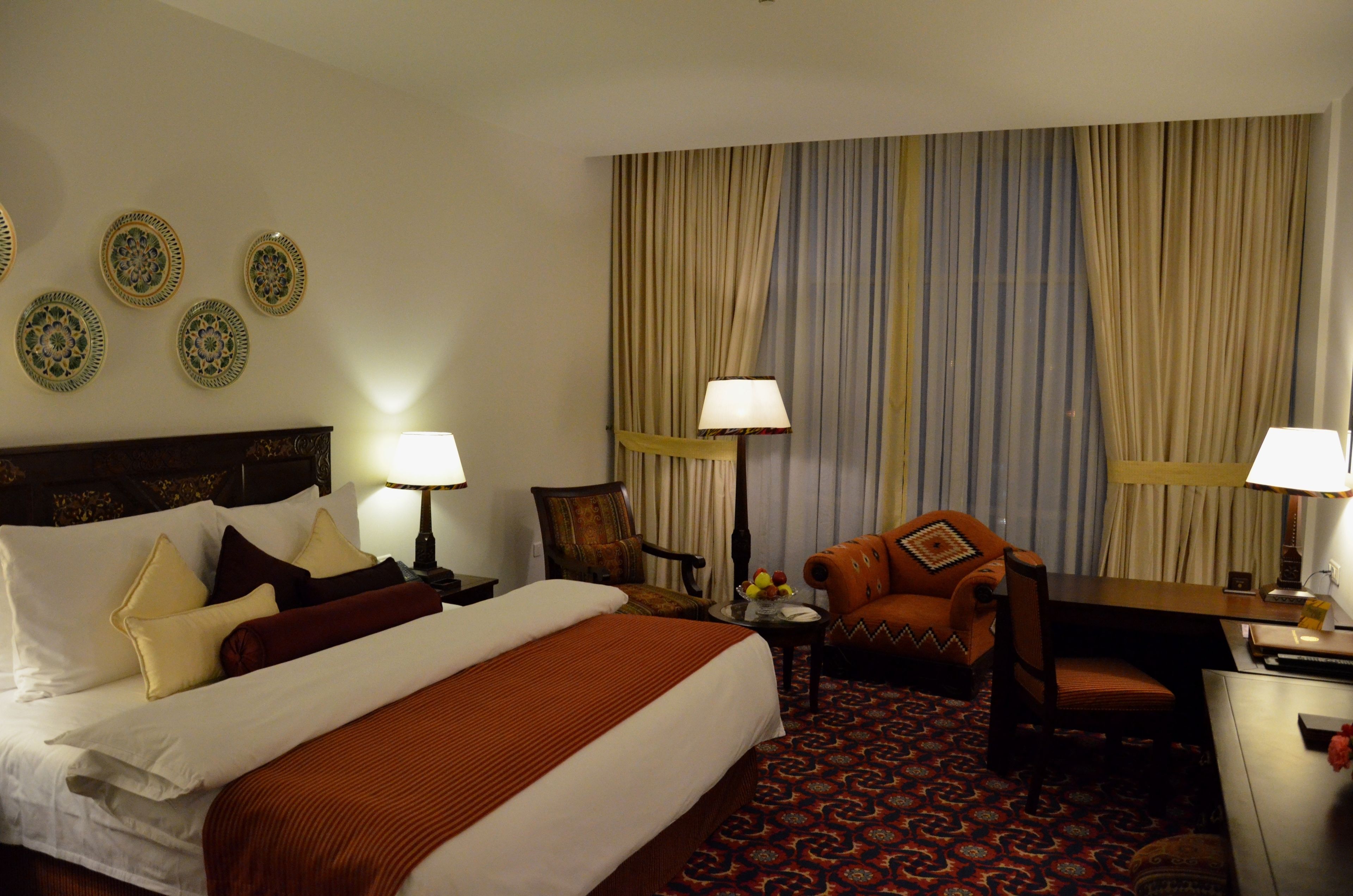 Une chambre d’hôtel avec un grand lit, deux chaises, un bureau et une table avec une lampe.
