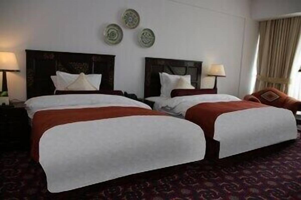 A hotel room with two beds, a dark headboard, a red carpet, and a lamp on the nightstand.
