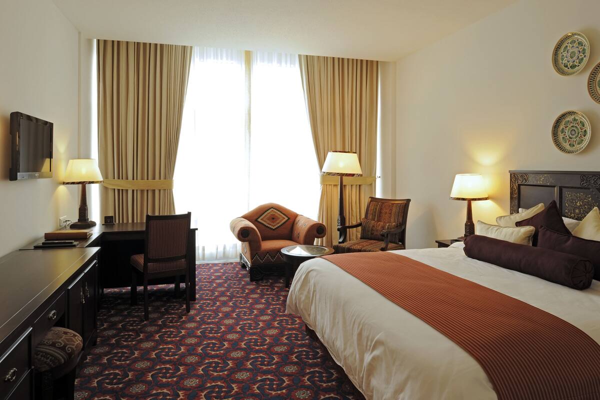 A hotel room with a large bed, two armchairs, a desk with a lamp, and a television.