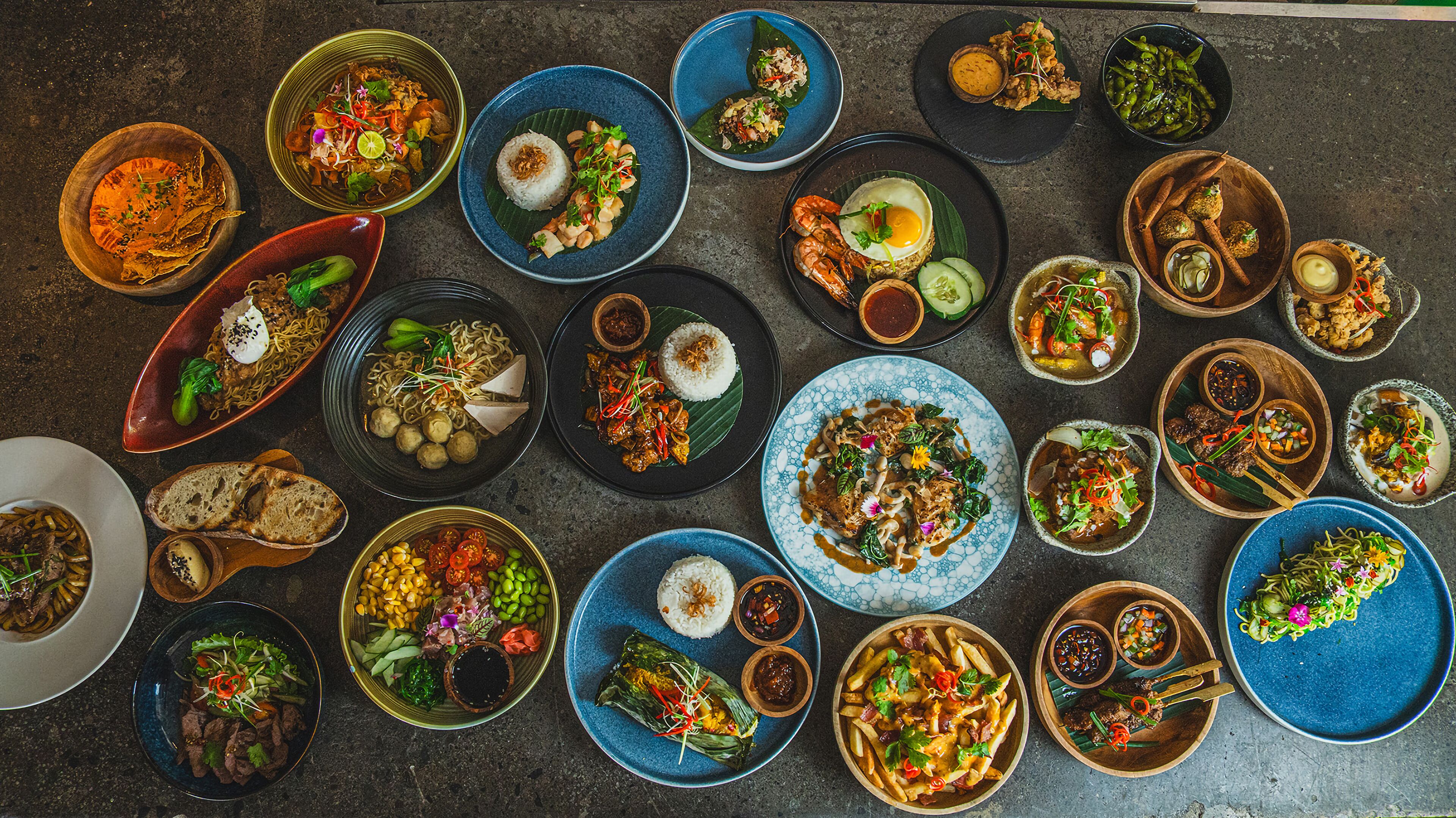 Une variété de plats disposés sur une table, notamment du riz, des nouilles et différentes sortes de salades.