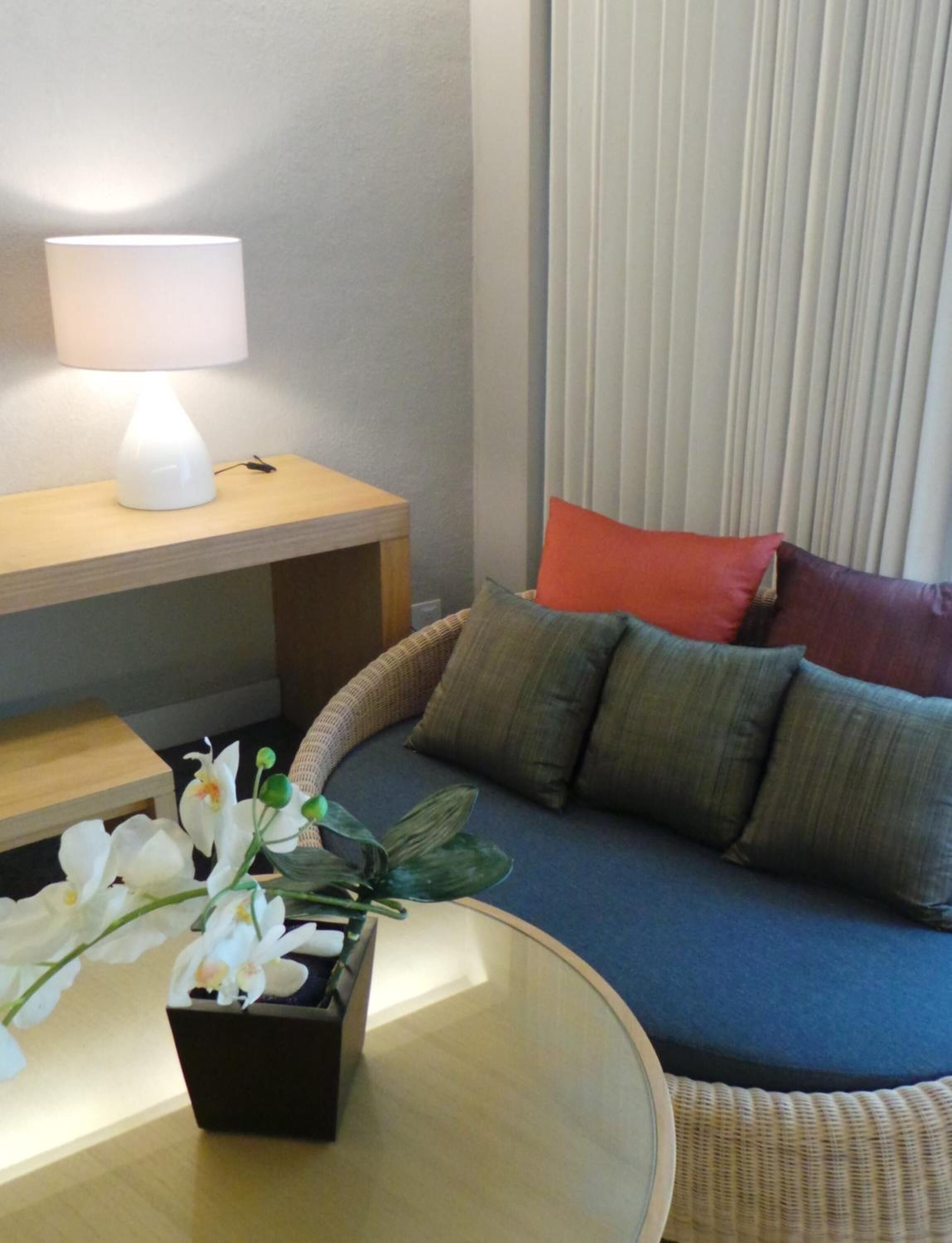 A modern living room with a sofa, cushions, a small table with a lamp, and a potted plant.