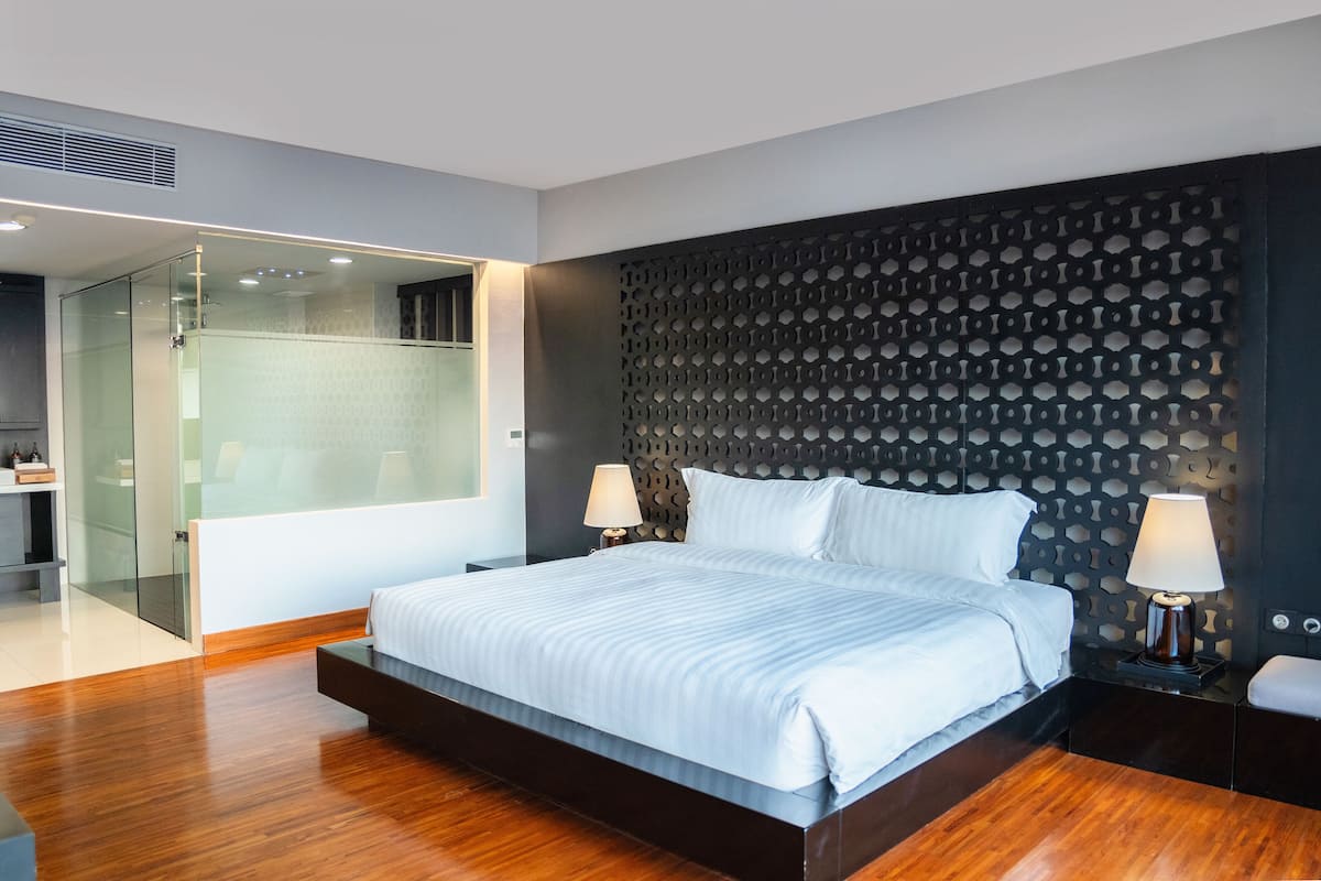 A modern hotel room with a large bed, a glass shower enclosure, and a dark patterned headboard.