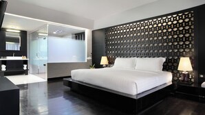 A modern hotel room with a large bed, a glass shower enclosure, and a decorative wall panel. - Cross Paasha Bali Seminyak (Seminyak)