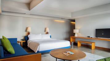 Una habitación de hotel moderna con cama, sofá azul, una pequeña mesa redonda, televisor y dos lámparas de noche.