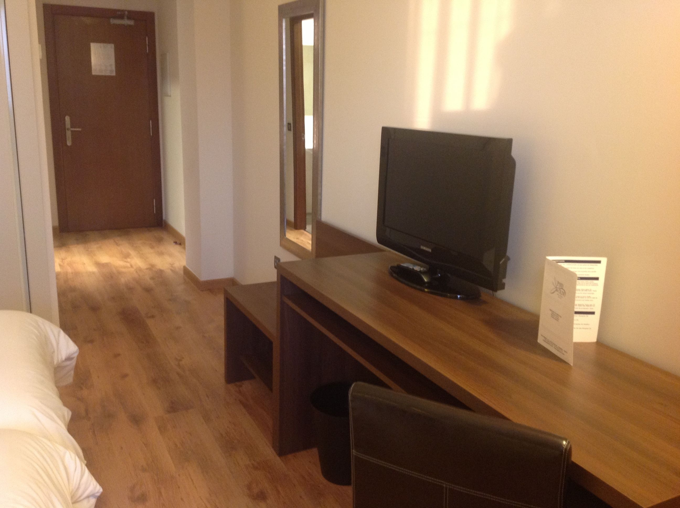 A hotel room with a wooden desk, a television, a mirror, and a bed.