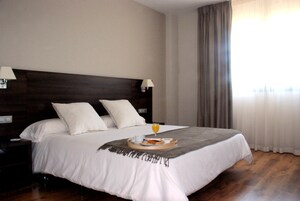 Cama bem arrumada com uma bandeja de itens de café da manhã, luminária ao lado da cama e vista para o exterior através de uma janela com cortinas.