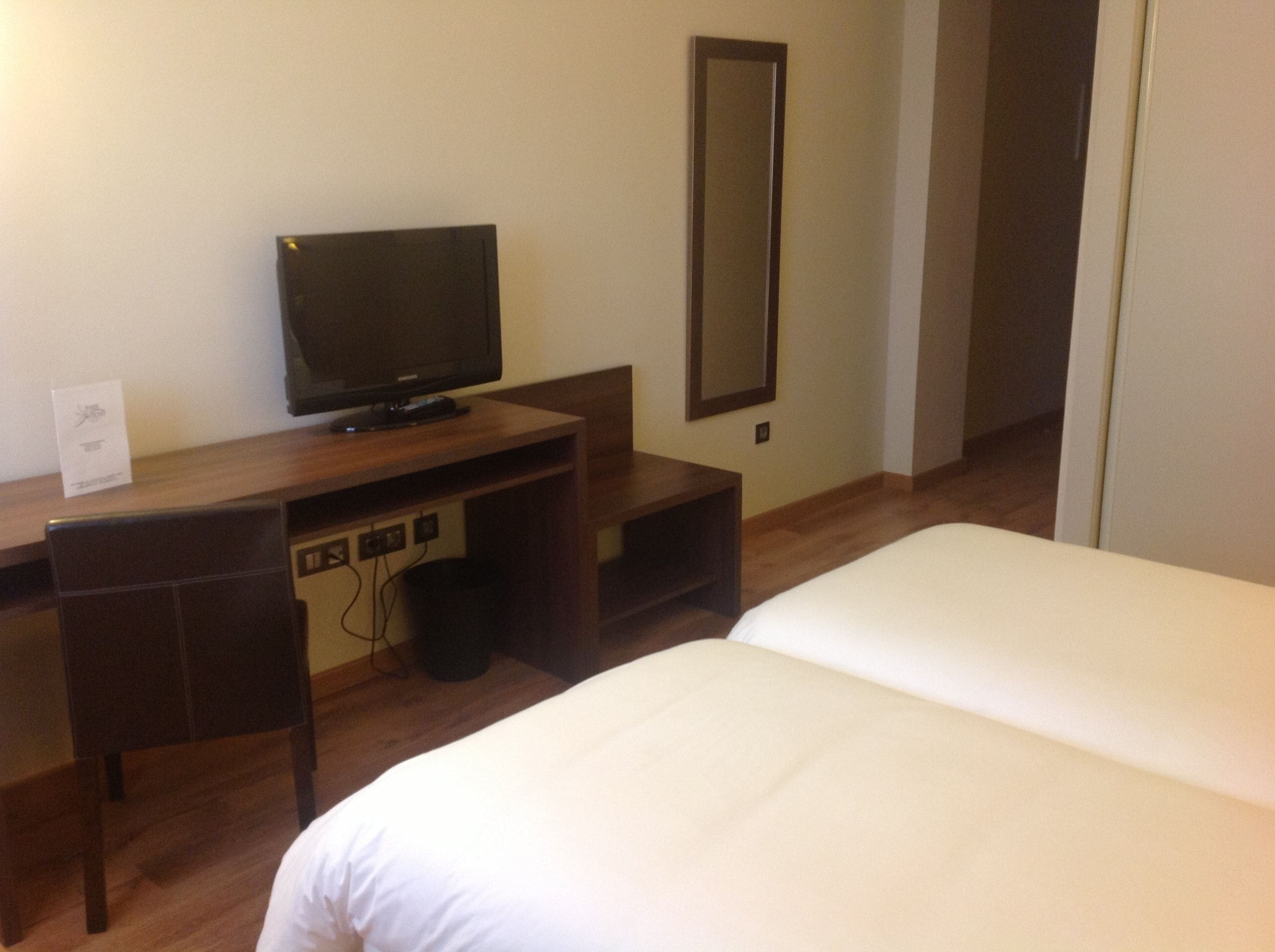 Una habitación de hotel con una cama, un escritorio con televisor y un espejo.