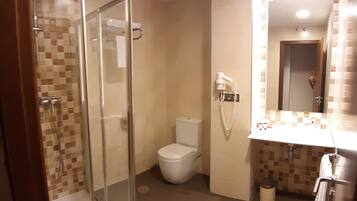A bathroom with a glass-enclosed shower, a toilet, and a sink with a mirror.
