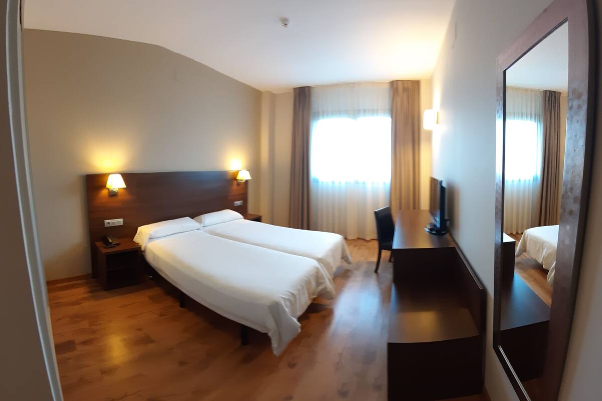 A hotel room with two beds, a desk, a chair, and a TV.