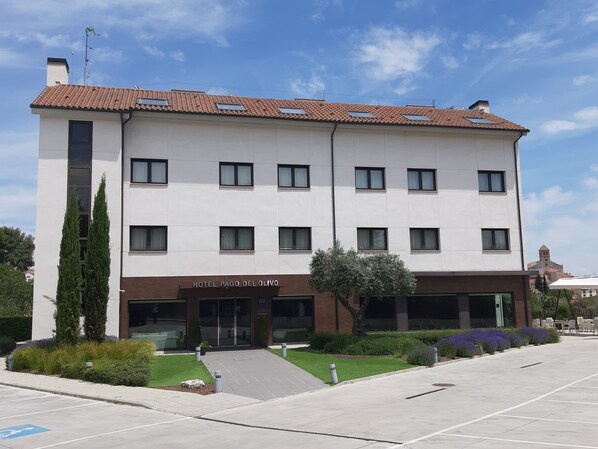 Un hotel con fachada moderna, varias ventanas y un cartel que dice "HOTEL PAGO DEL OLIVO".