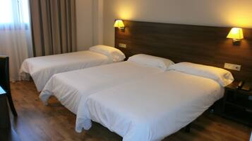 Habitación de hotel con dos camas individuales, suelo de madera, una mesita de noche con lámpara y una ventana con cortinas.