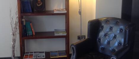 Una habitación con un sillón de cuero negro, una estantería de madera y una lámpara de pie.