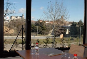 Uma mesa com uma garrafa de água e um copo, uma cadeira, e vista para um edifício com cúpula e árvores ao primeiro plano.