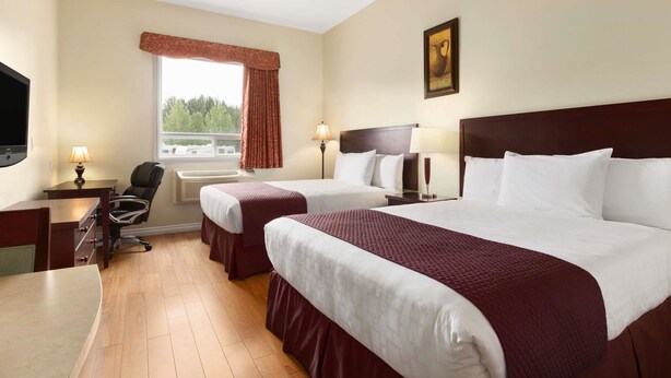 Ein Hotelzimmer mit zwei Betten, einem Schreibtisch, einem Stuhl, einem Fernseher und einem Fenster mit Vorhängen.